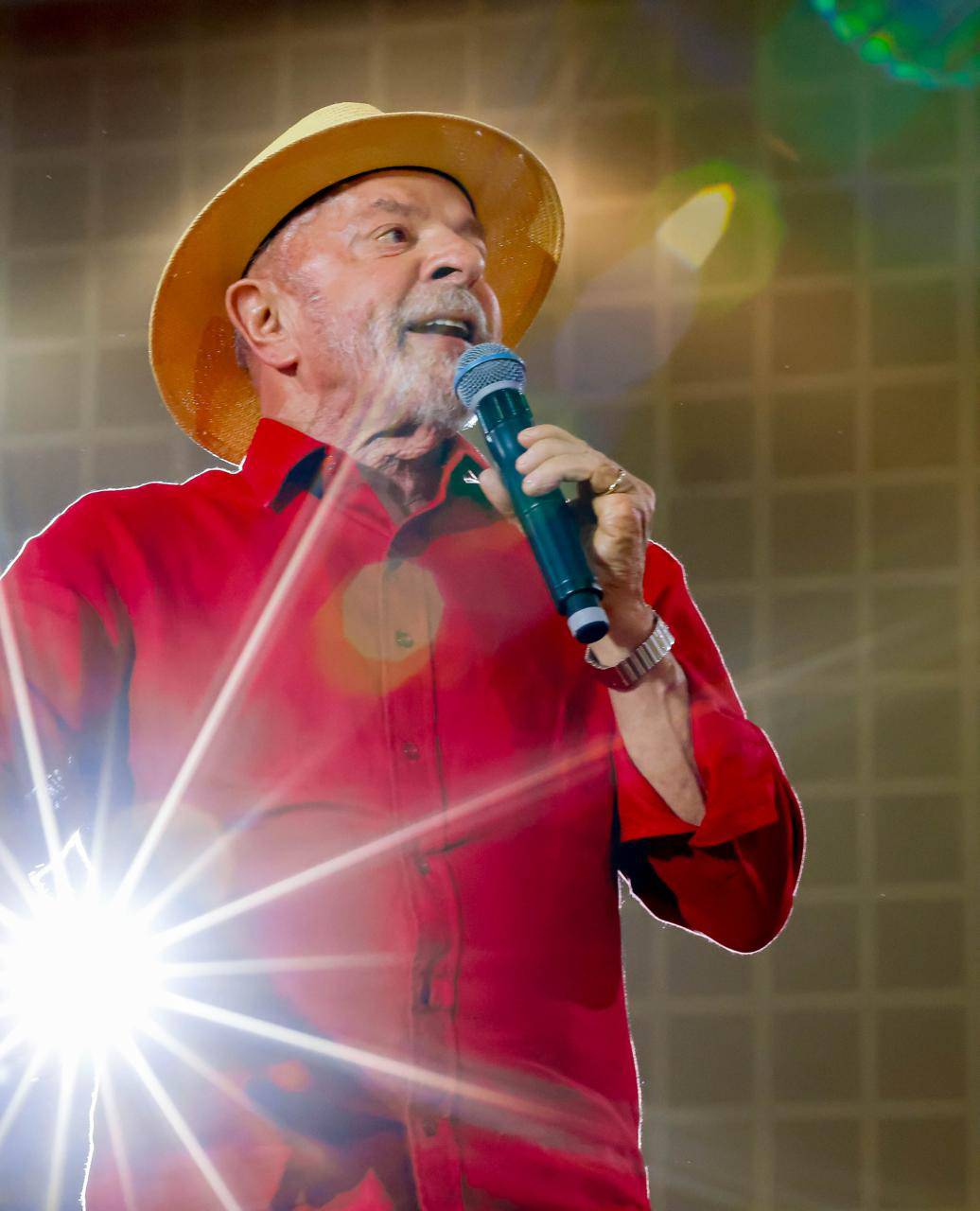 Lula, de camisa vermelha e chapéu, fala ao microfone em um palco