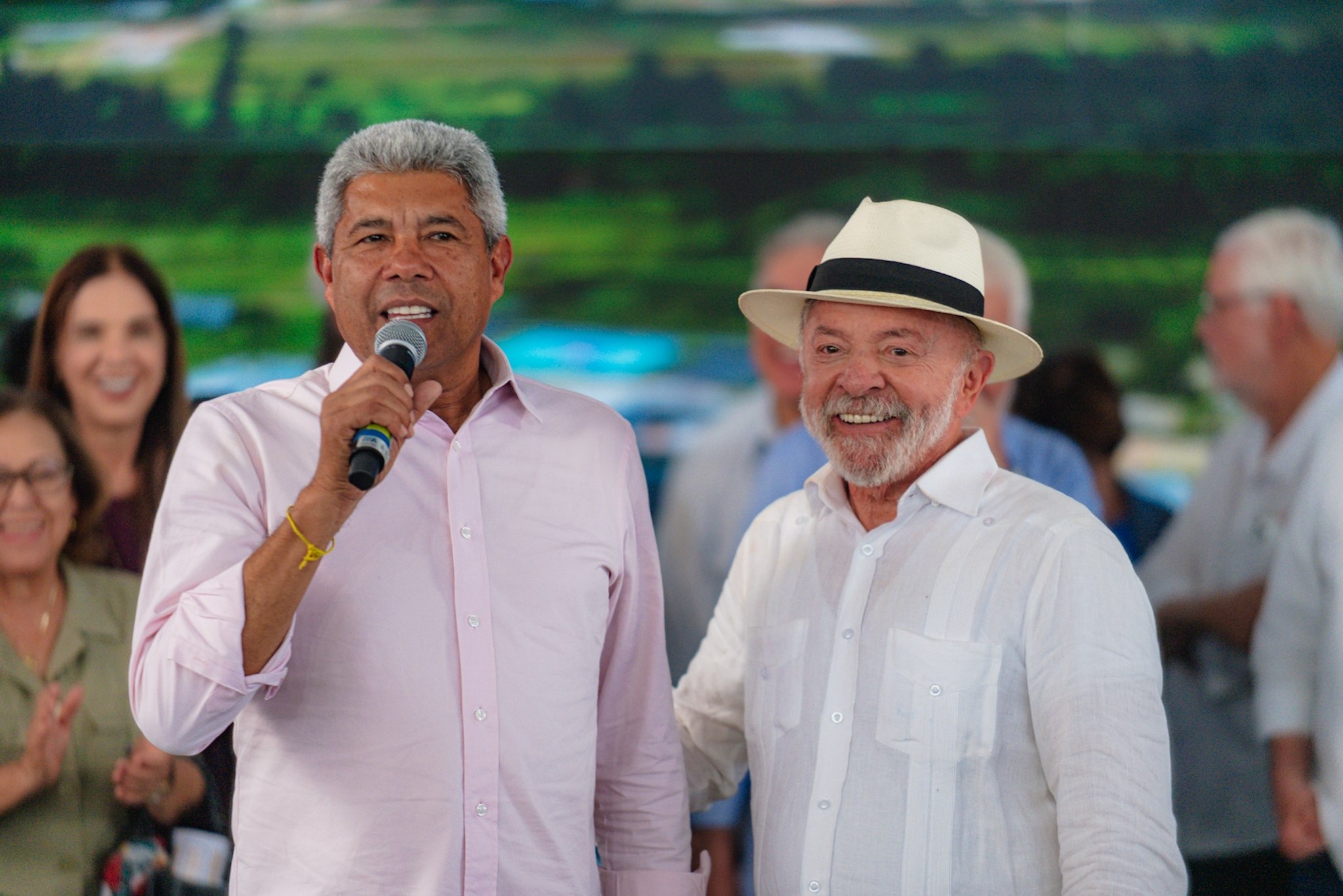 Jerônimo Rodrigues fala ao microfone ao lado de Lula, que usa um chapéu claro