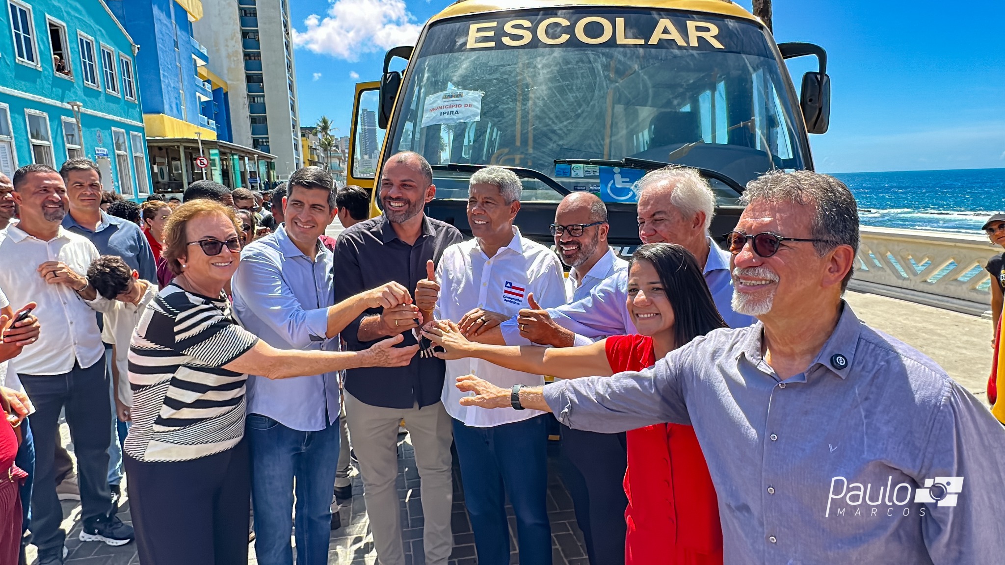 Participantes da cerimônia reunidos com uma chave diante de um ônibus escolar