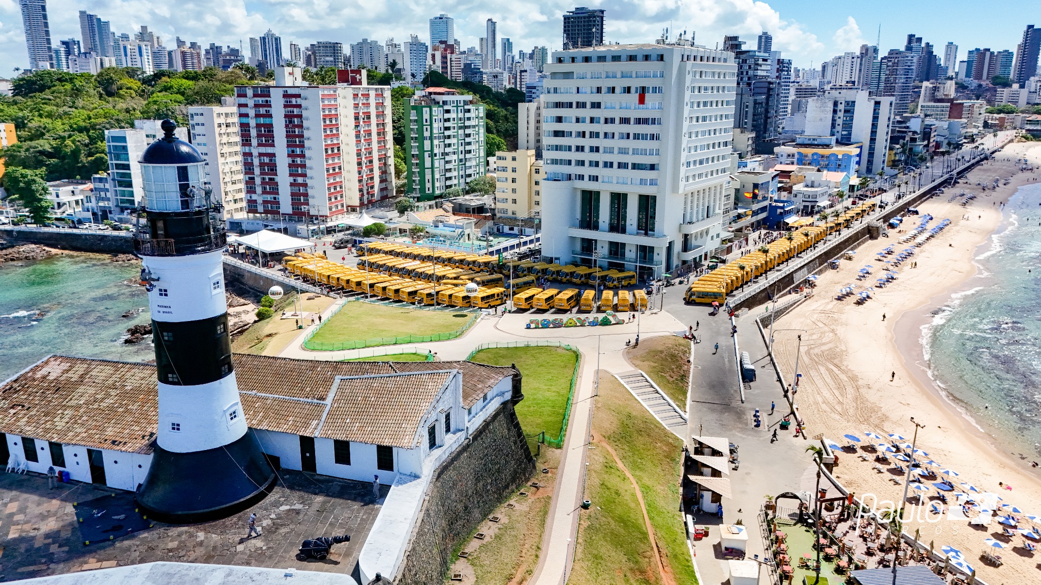 Vista aérea do Farol da Barra com a frota de ônibus escolares reunida na orla