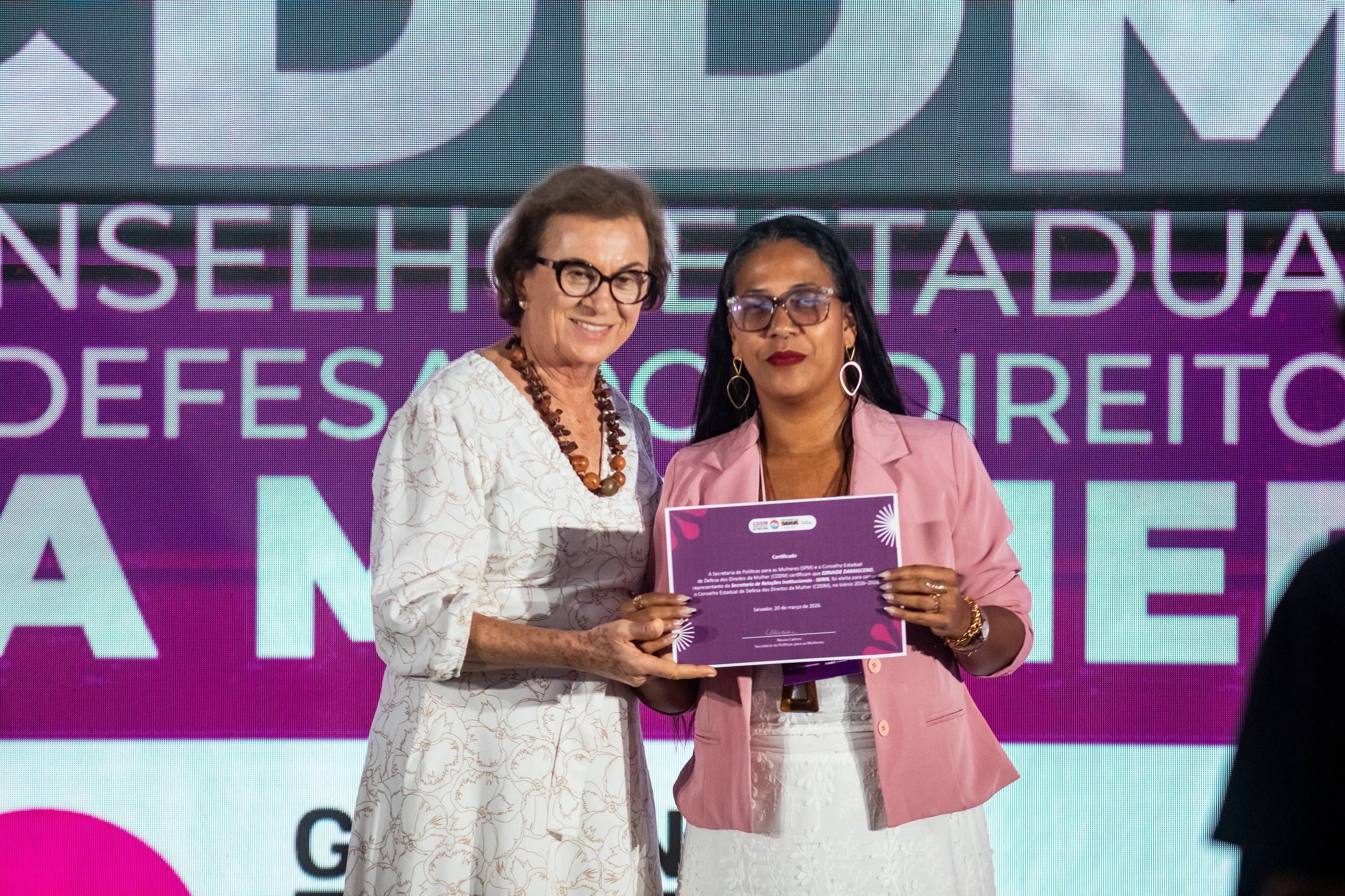 Neusa Cadore ao lado de uma participante, segurando um certificado em evento de políticas para as mulheres