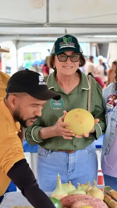 Neusa Cadore segura uma fruta diante de uma banca de alimentos